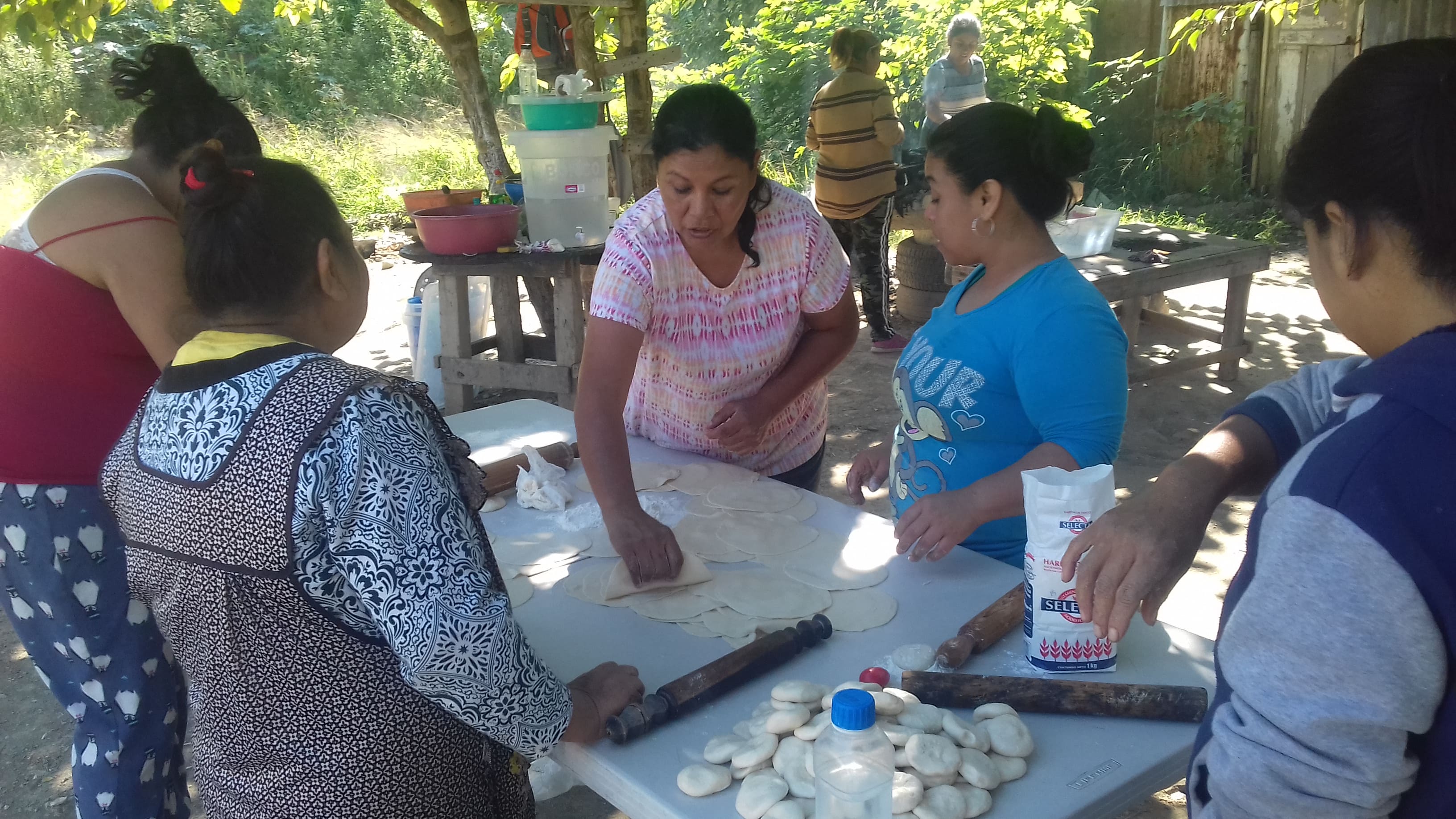 Supported family in northern Mexico standing outside their modest block home under warm sunlight.